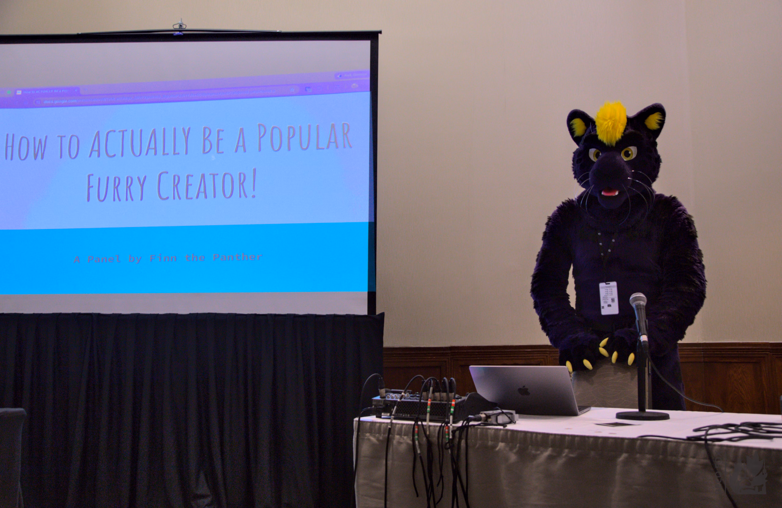 Finn the Panther, a purple panther fursuiter with yellow headfur, stands ready to present a panel. The screen says "How to Actually Be a Popular Furry Creator!"